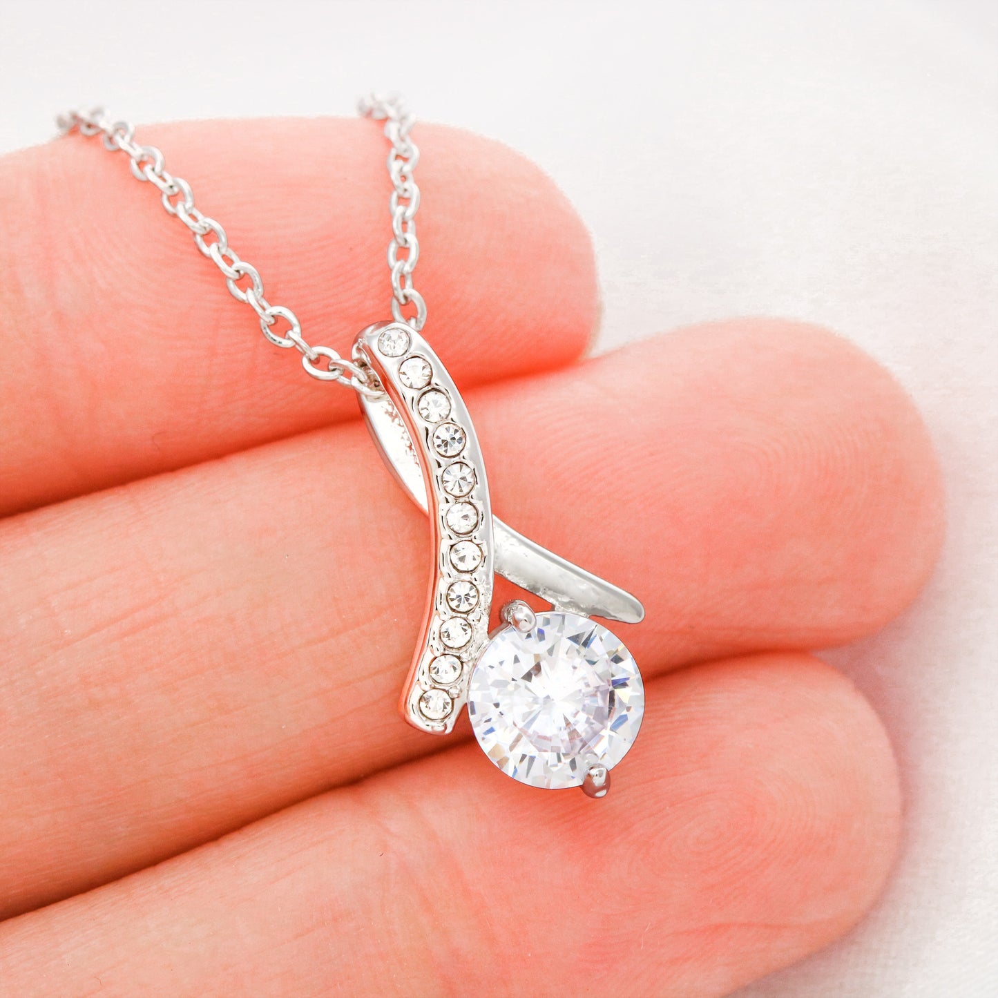 Silver necklace with a clear pendant held between fingers on a light background