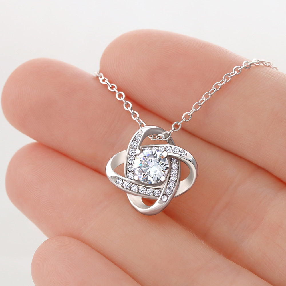 Silver necklace with a heart-shaped pendant held between fingers on a white background