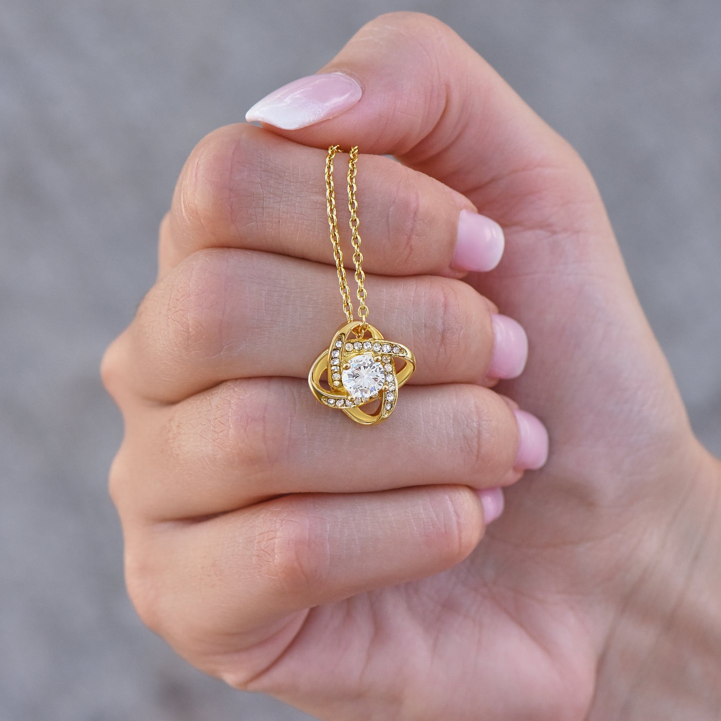 Gold finish necklace with a heart-shaped pendant held in a hand against a blurred background