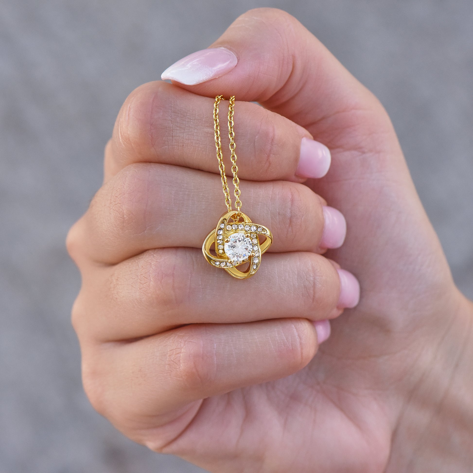 Gold finish necklace with a heart-shaped pendant held in a hand against a blurred background
