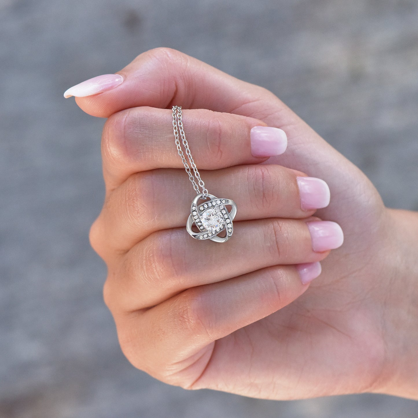 Hand holding a silver necklace with a zirconia pendant against a blurred background