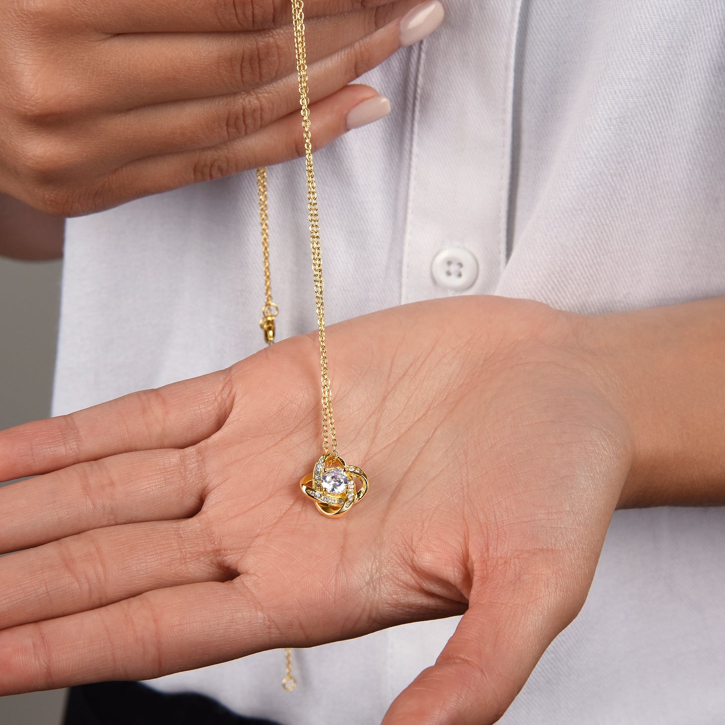 Gold finish necklace with a pendant held in a hand against a white shirt background